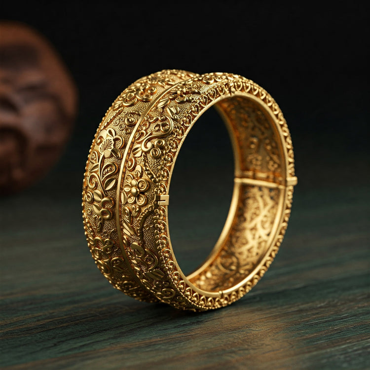 Detailed close-up of a Feelori Kada bangle with intricate traditional motifs in matte gold finish, on dark teak wood - heritage Indian jewelry.