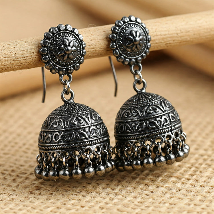 Pair of Feelori Oxidised Jhumka earrings with a textured, blackened silver finish on woven fabric - tribal-inspired Indian jewelry.