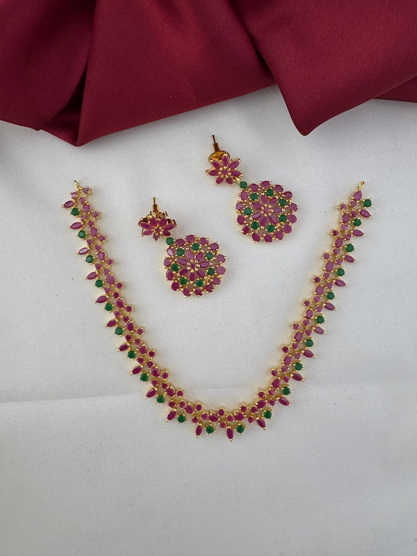 FeelOri Andhra Festive Gem Ruby & Emerald Short Necklace Set - Complete set view with necklace and earrings on a white and maroon background.