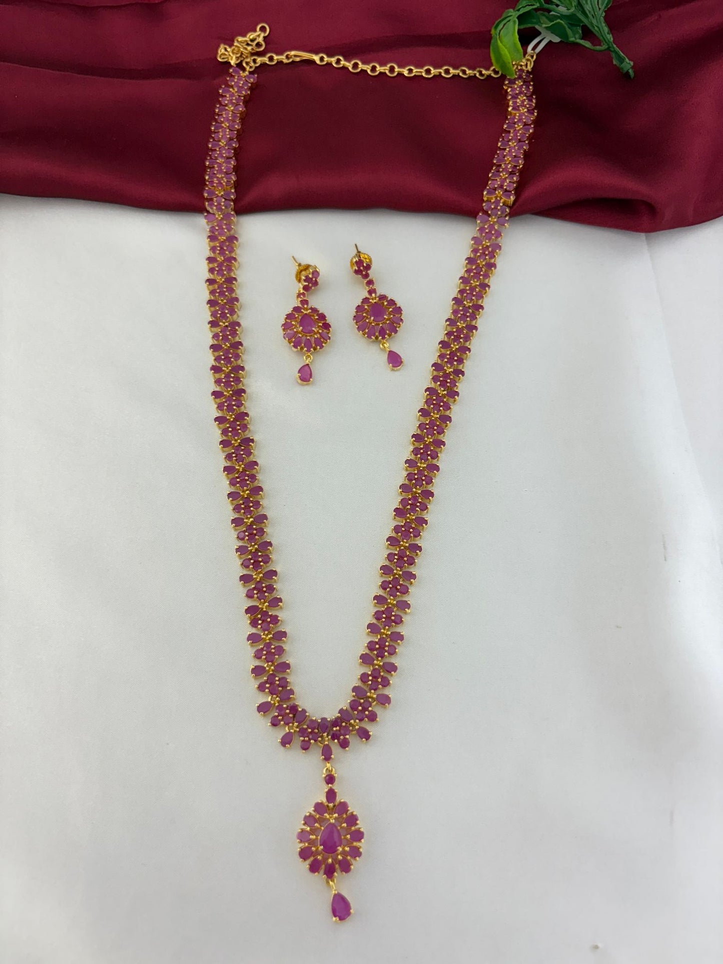 FeelOri Celestial Fire Ruby & AD Halo Long Necklace & Earring Set - Full view on maroon and white background.