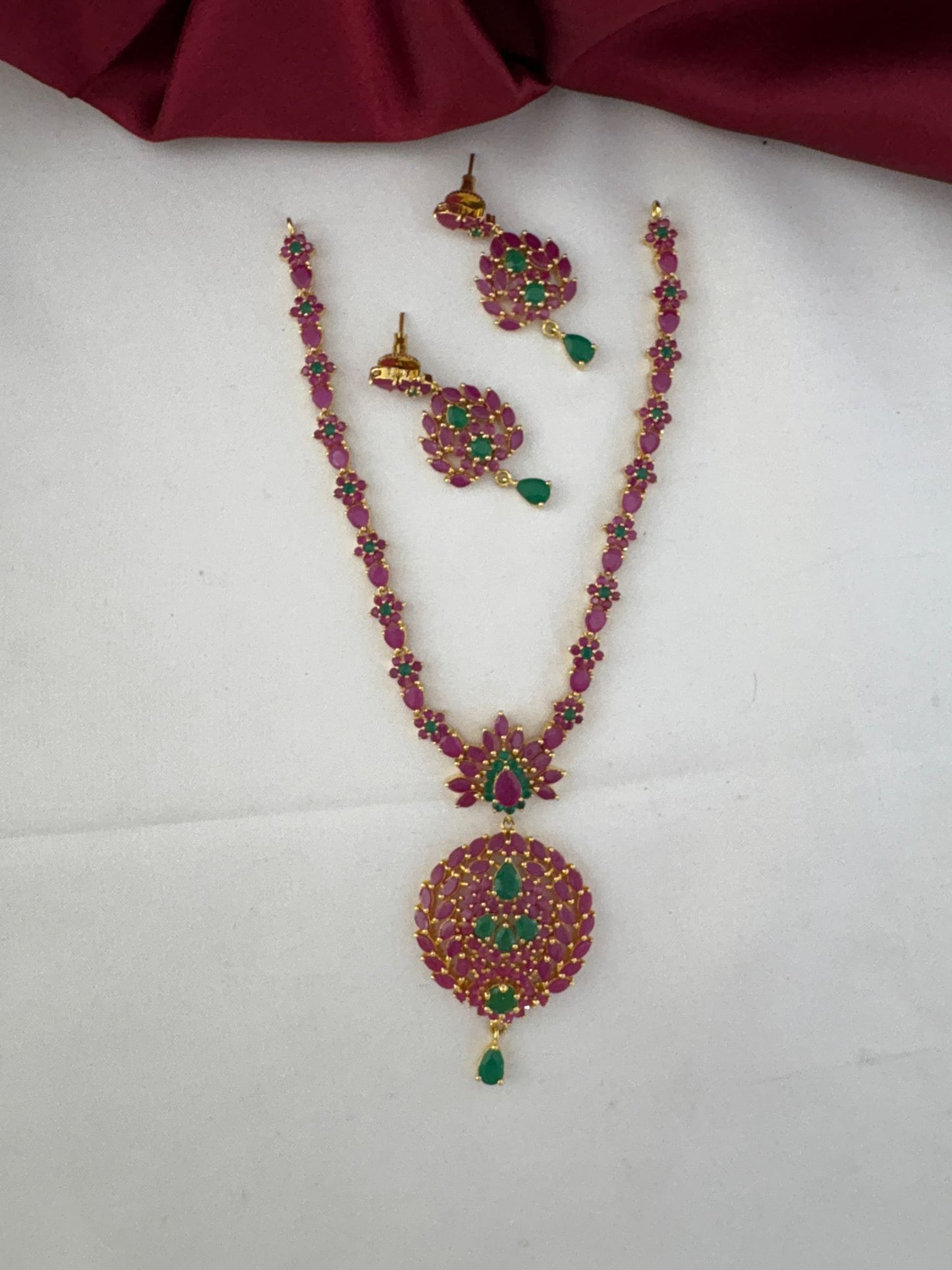 FeelOri Classic Duo Ruby & Emerald Short Necklace Set with matching earrings, top view on a white and maroon background.