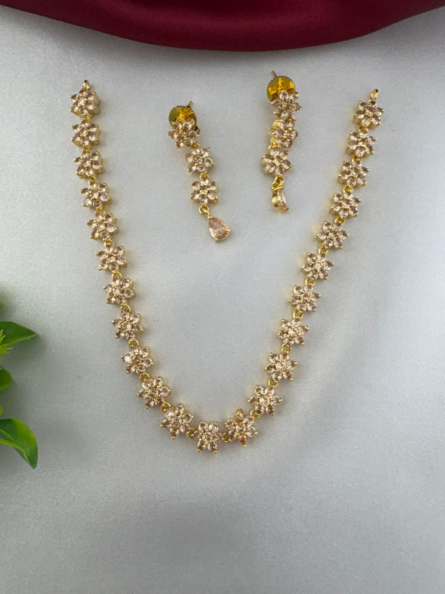 feelori Classic Gold Sparkle AD Short Necklace and Earrings Set, floral design, shown on a light grey surface with a rich burgundy cloth.