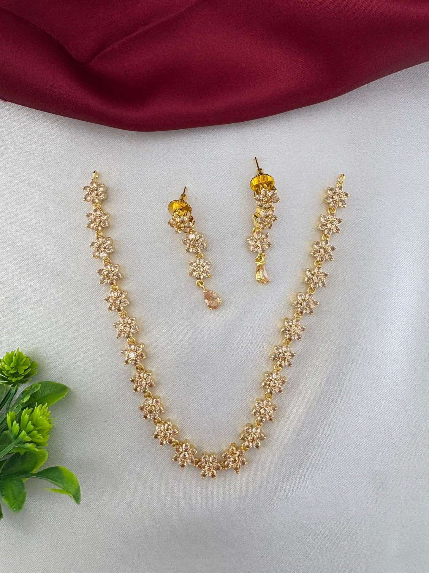 feelori Classic Gold Sparkle AD Short Necklace Set displayed on a white surface with burgundy satin and green foliage.