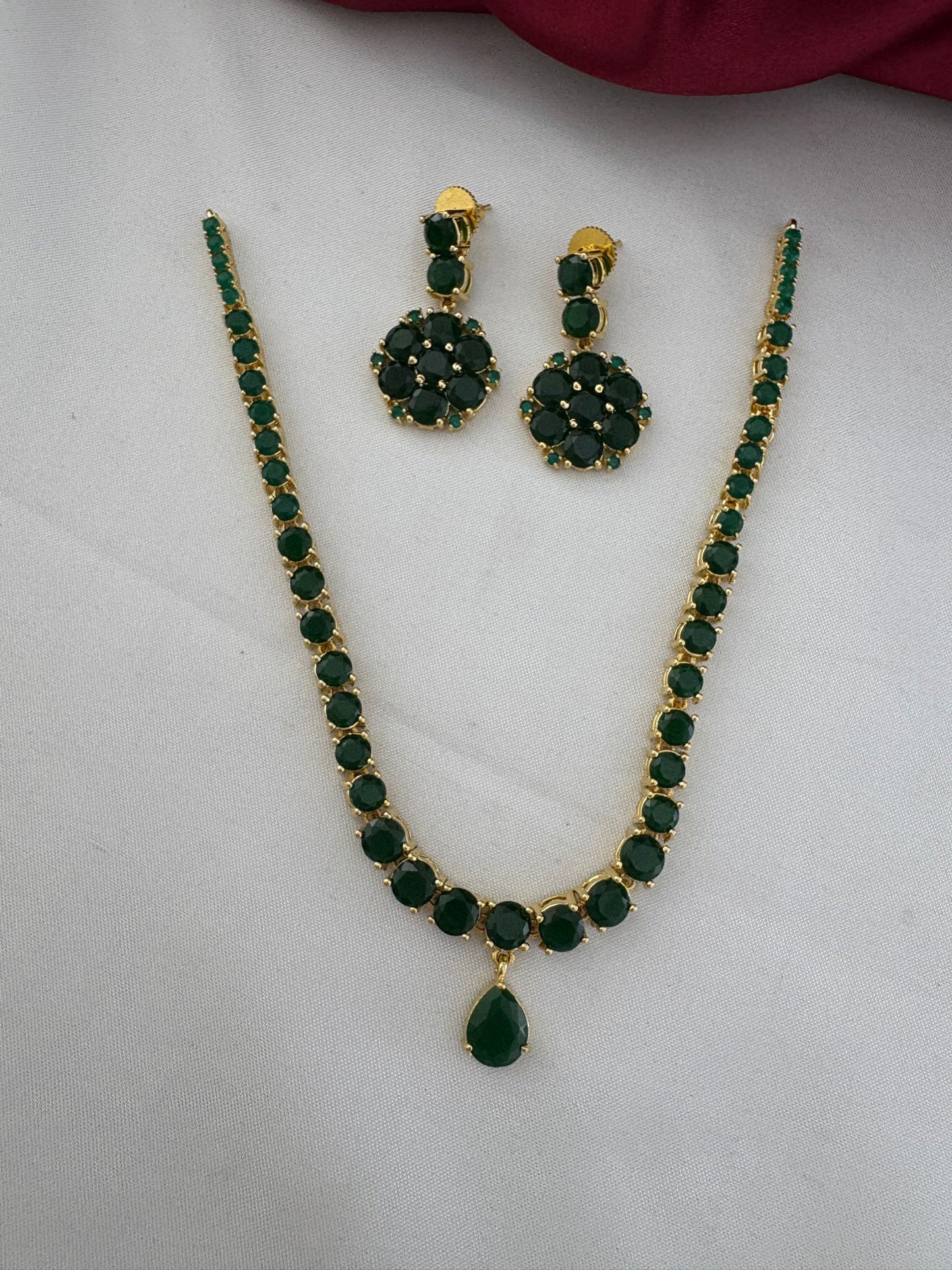FeelOri Deccan Spring Emerald Short Necklace Set - Main view of the necklace and matching earrings with green stones laid flat against a white and maroon background.