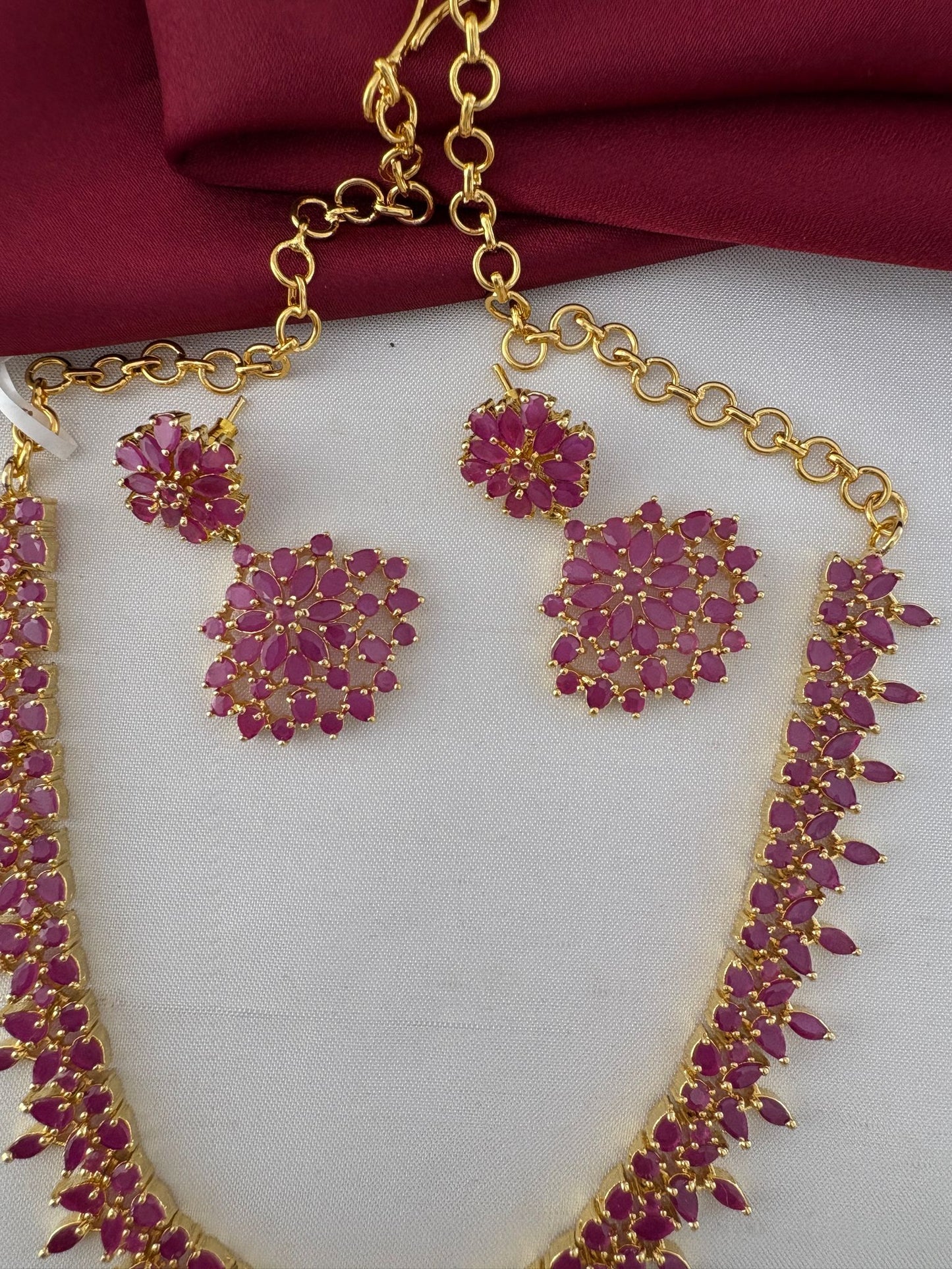 Close-up detail of the Feelori Gorgeous Original Ruby Short Necklace and Earrings set, showcasing the intricate ruby stone work and gold plating.