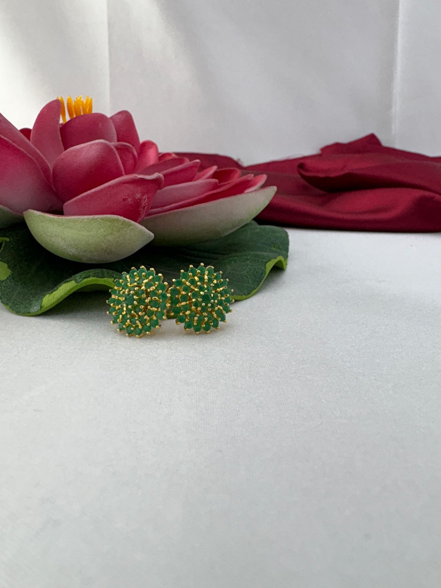 FeelOri emerald green AD stud earrings styled with pink lotus flower creating elegant contrast on fabric backdrop
