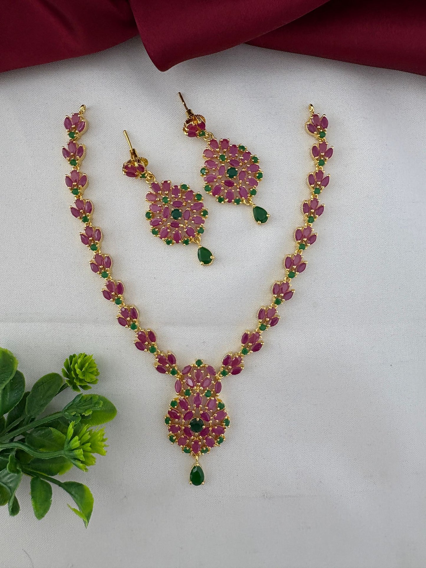 FeelOri Kerala Temple Duo Ruby & Emerald Necklace Set with decorative plant accent.