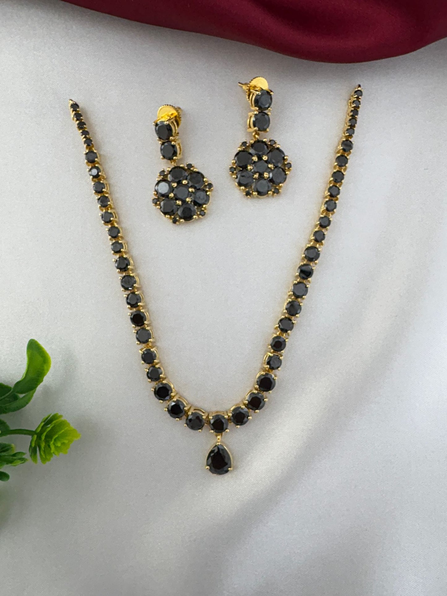 Top view of FeelOri Midnight Glam Black AD Short Choker Set and earrings. Elegant evening wear necklace set by feelori, on a white satin background.