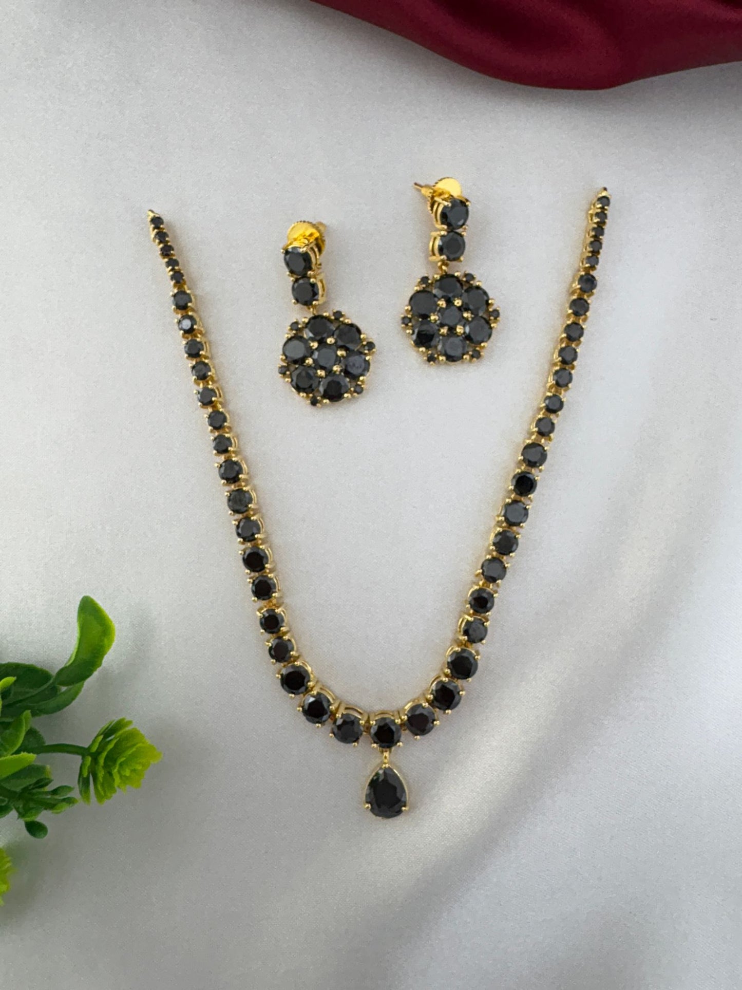FeelOri Midnight Glam Black AD Short Choker Set with matching earrings. Full view displayed on a white satin surface with red and green accents. Evening wear jewellery by feelori.