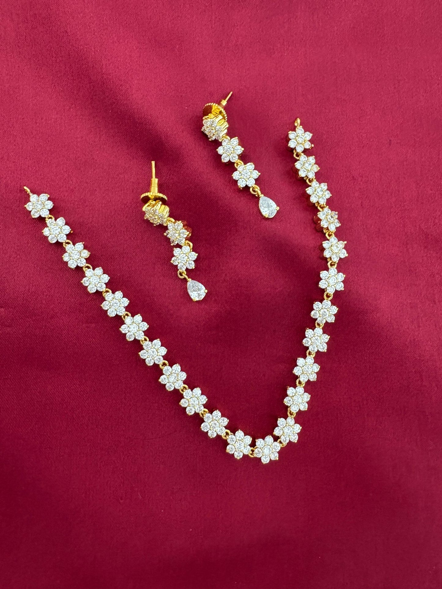 FeelOri Solitaire Sparkle AD Stone Short Necklace Set, detailed view of floral links and earrings on maroon.