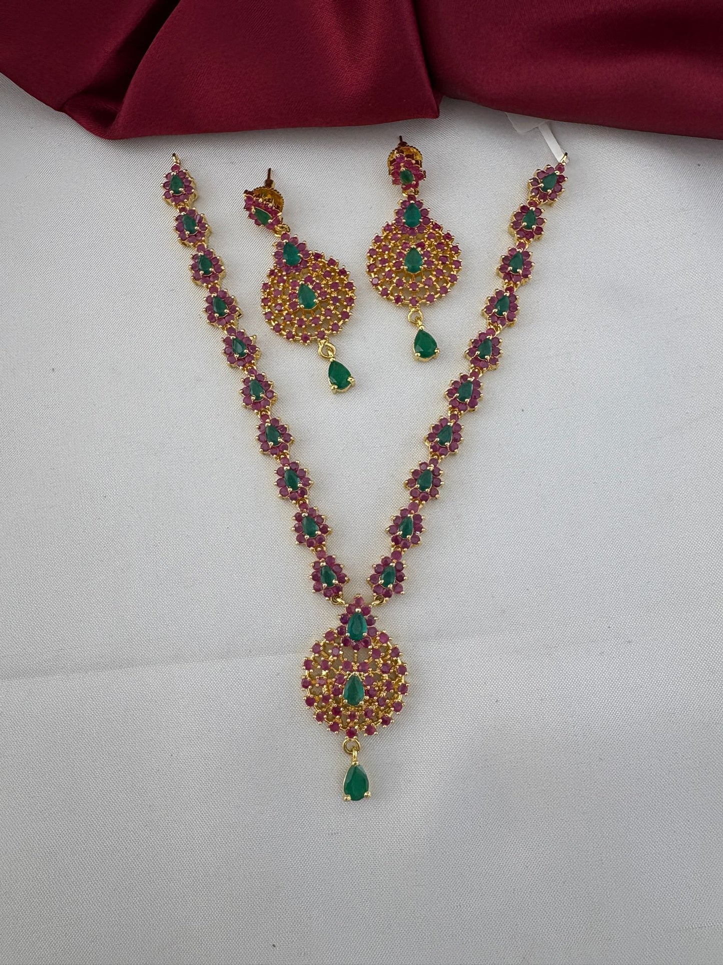 FeelOri Tamil Heritage Twin Stone Ruby & Emerald Short Set - Necklace and Earrings full view on white and maroon background.