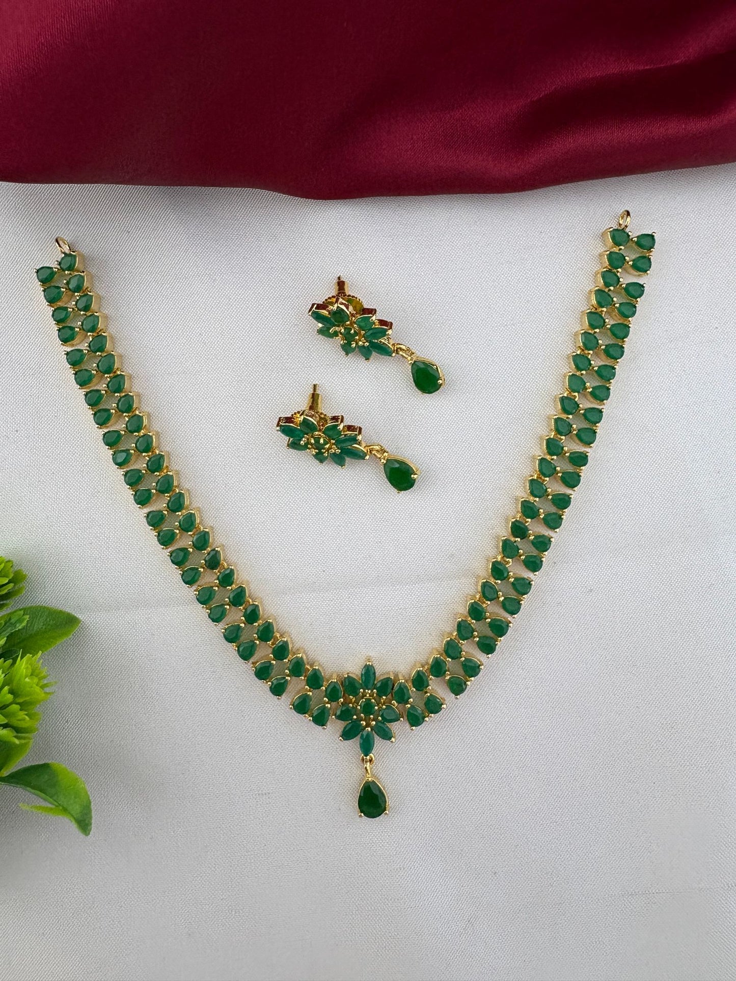 The complete FeelOri Urban Oasis Minimalist Emerald Pendant Set, including necklace and earrings, styled with a subtle green plant accent, perfect for daily chic wear.