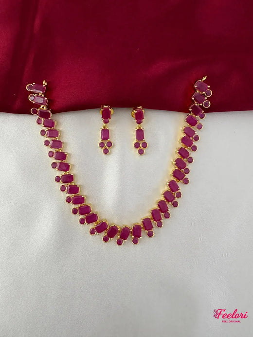 FeelOri Gold Plated Ruby Geometric Necklace Set - Full view showcasing the necklace and matching earrings laid out on a white and maroon fabric.