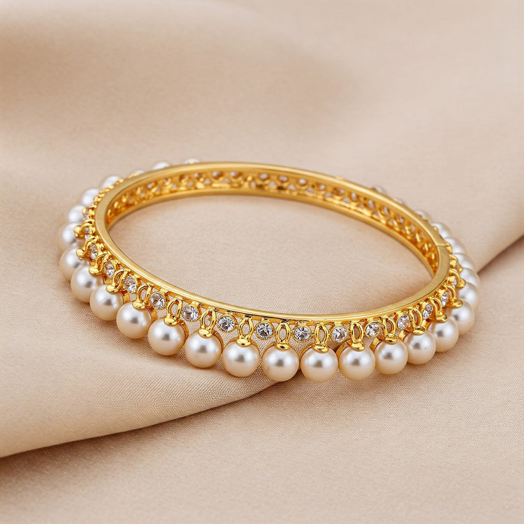 Elegant Feelori bangle featuring lustrous real pearls set in gold plate, resting on soft oyster silk - classic Indian jewelry.