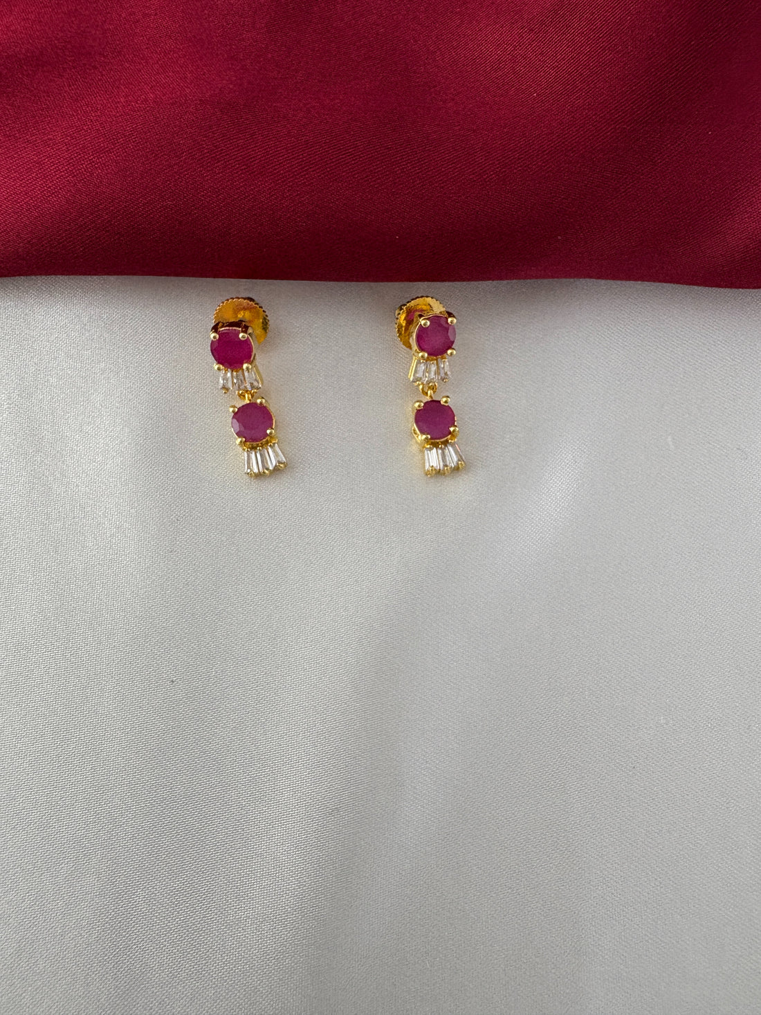 FeelOri Gold Plated Ruby Baguette Earrings - Detailed view of the matching drop earrings featuring three ruby hued circular stones and baguette clear stones.