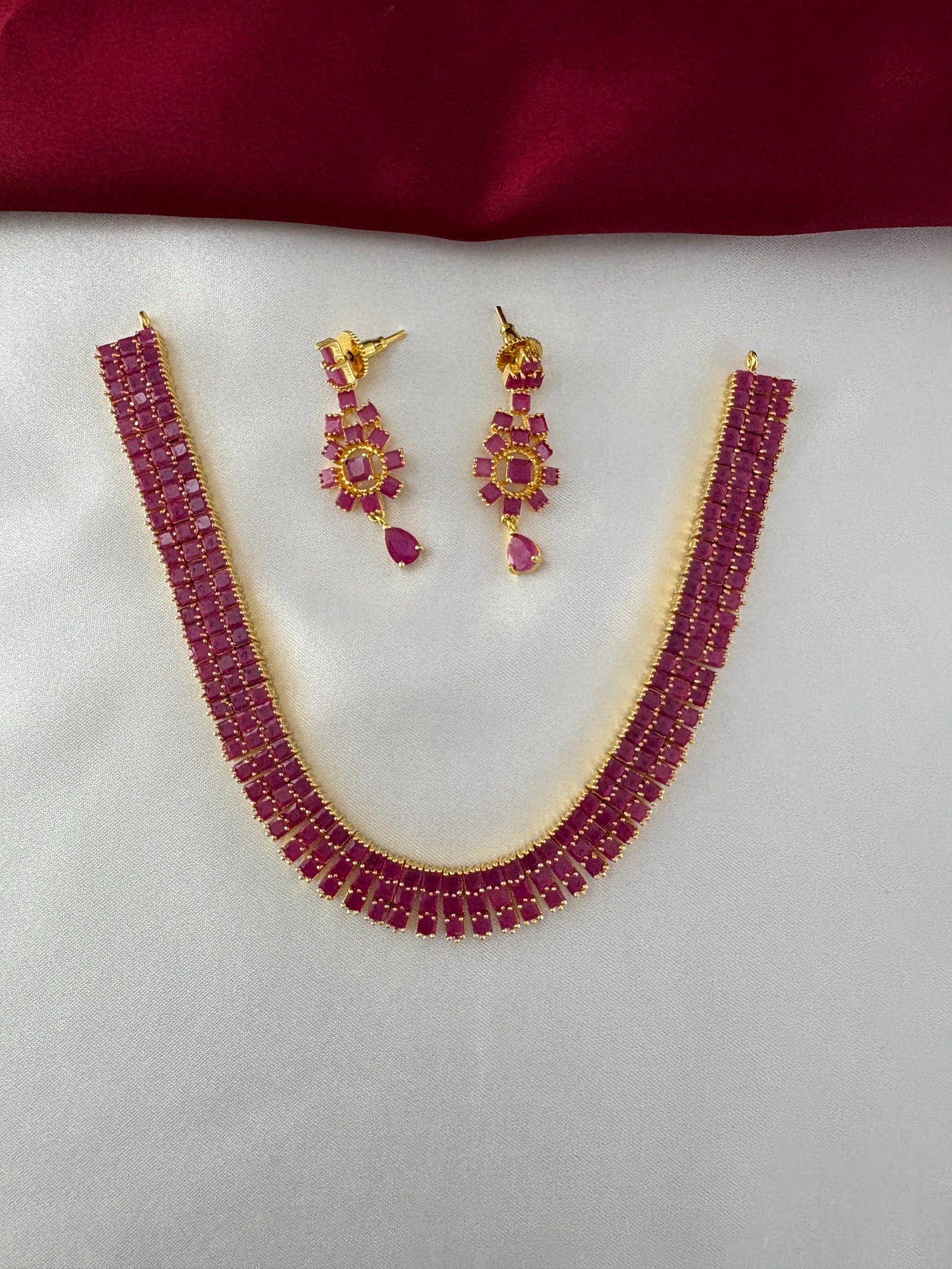 FeelOri Gold Plated Ruby Bar Necklace & Earring Set - Top view showcasing the full elegant set on a white silk backdrop.