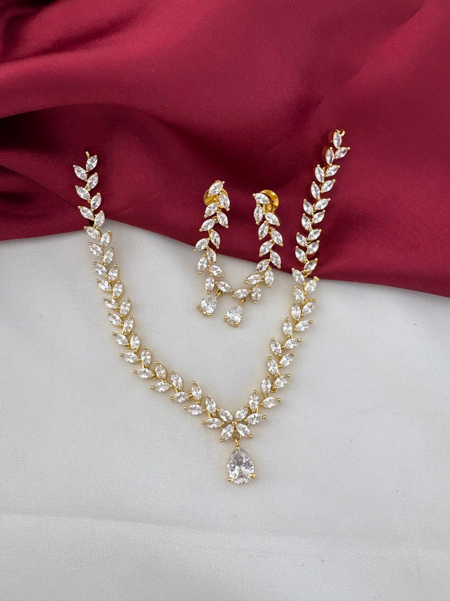 FeelOri Festive Dazzle AD Stone Floral Short Necklace and Earrings Set, elegantly displayed on maroon and white satin.