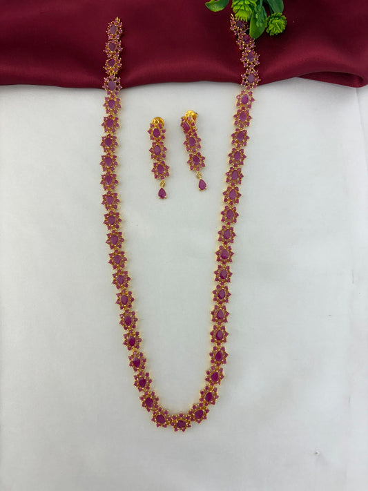 FeelOri Geometric Glow Ruby Station Long Necklace & Earring Set - Styled overview shot of the ruby necklace and earrings with a decorative green element.