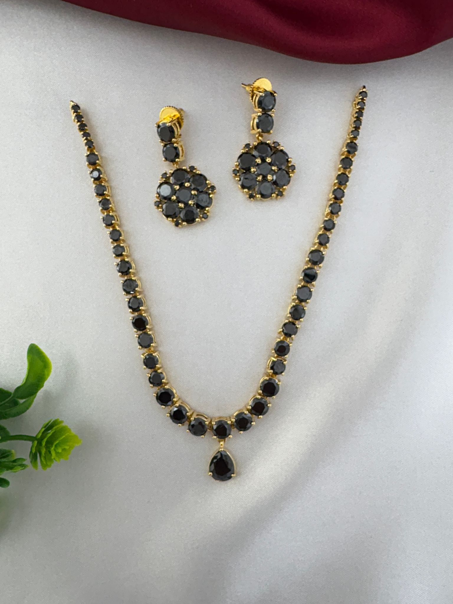 Top view of FeelOri Midnight Glam Black AD Short Choker Set and earrings. Elegant evening wear necklace set by feelori, on a white satin background.