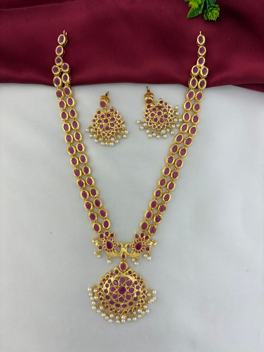 FeelOri Royal Crimson Cascade Ruby Long Necklace and Earring Set. Features an angled view of the ornate pendant with rubies and pearls, and matching earrings. Displayed on a white and rich maroon fabric.
