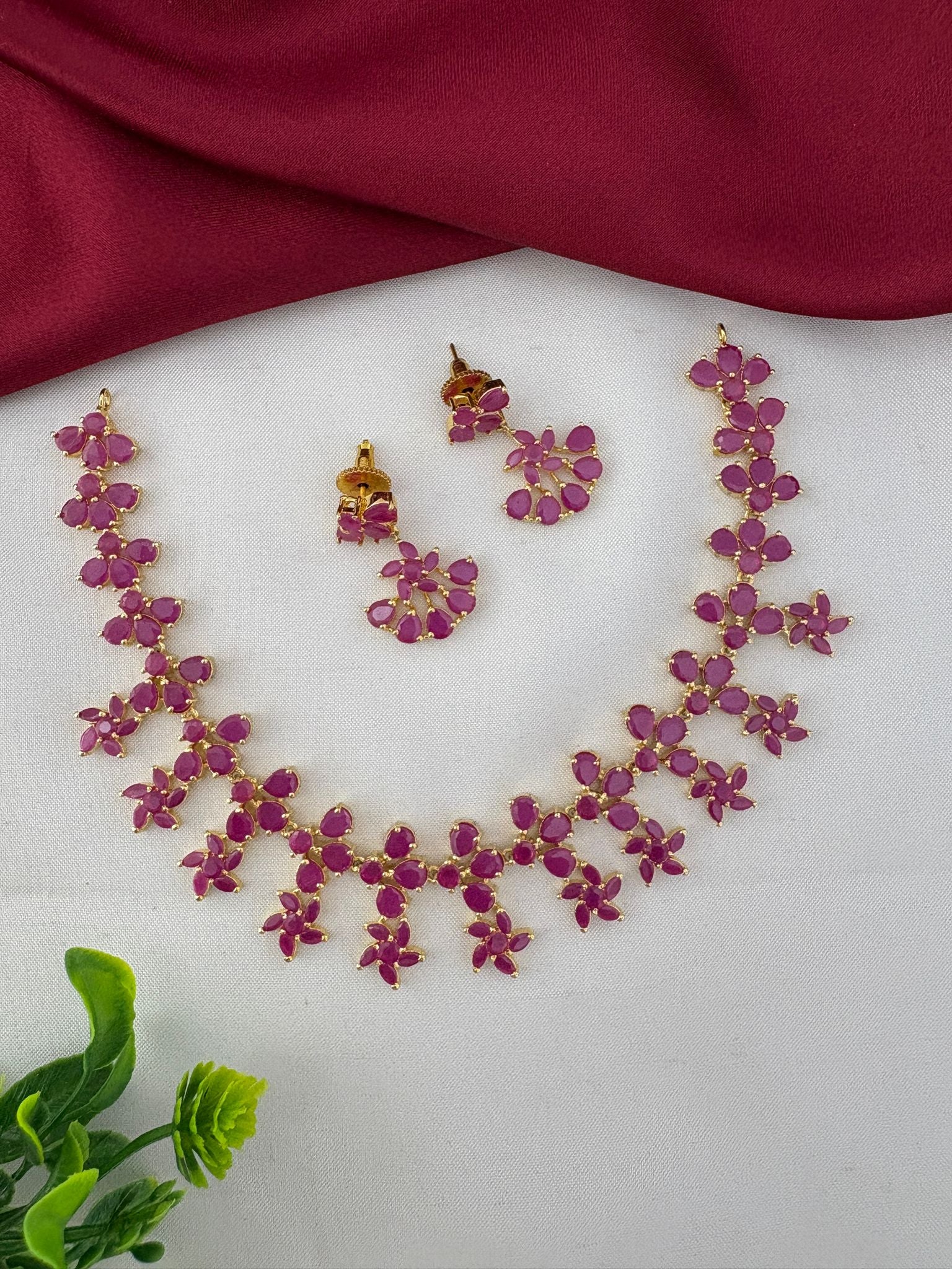 FeelOri Exclusive Ruby-Tone CZ Short Necklace Set - Designer Wear - Styled view with earrings and decorative leaf.