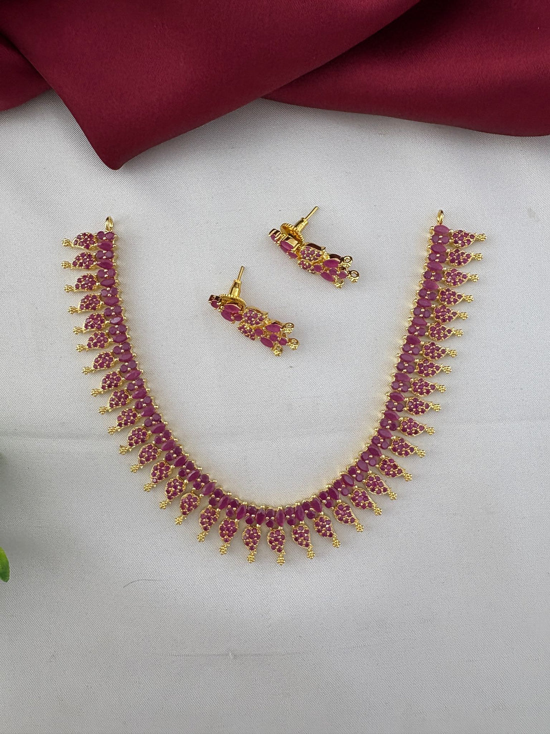 FeelOri Bridal Wear Ruby-Tone CZ Short Necklace Set - South India Special - Angled view of the ruby necklace and matching earrings laid flat.