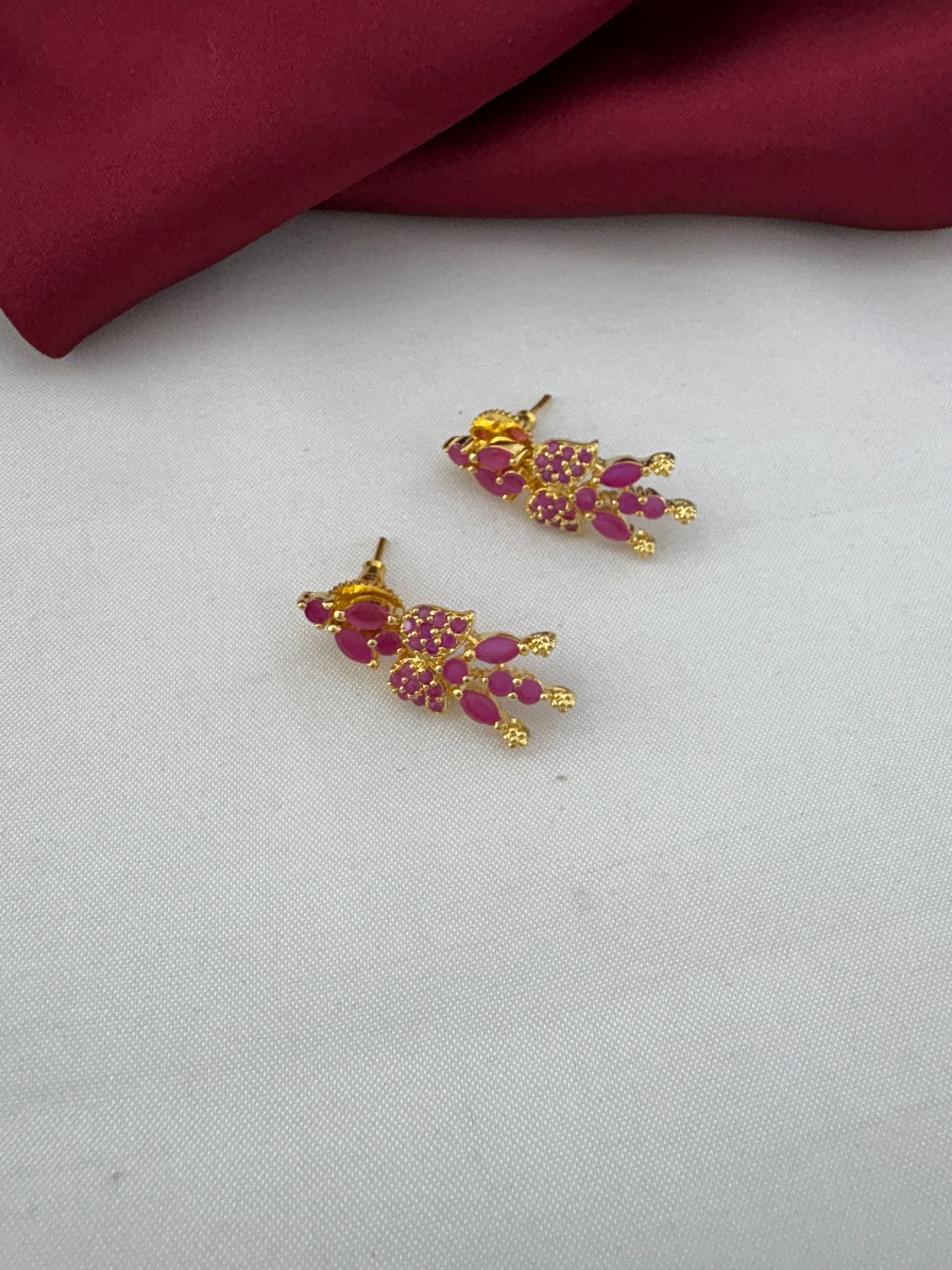 FeelOri Bridal Wear Ruby-Tone CZ Short Necklace Set - South India Special - Close-up of ruby stud earrings on a white and maroon background.