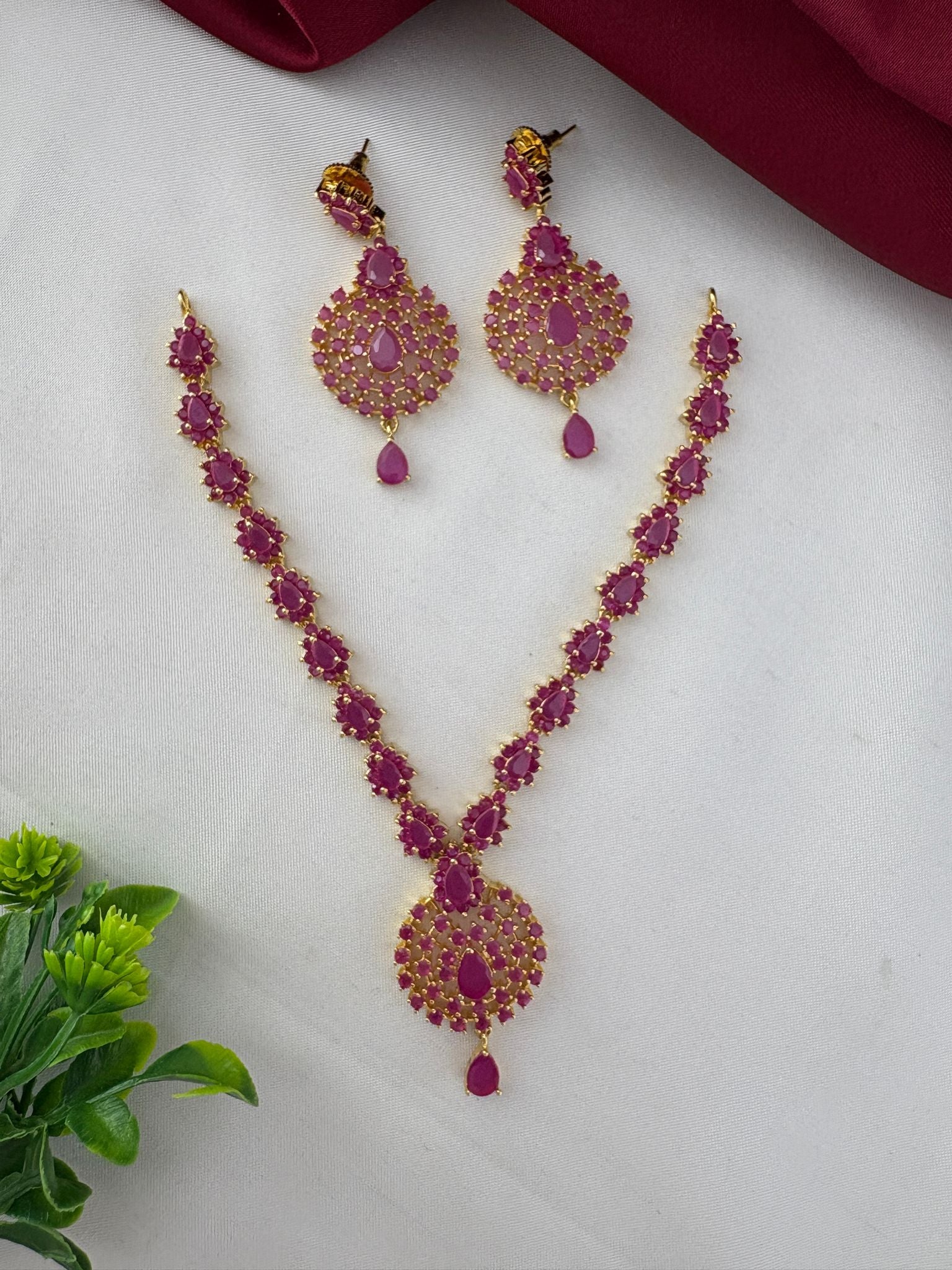 FeelOri Stunning Ruby-Tone CZ Short Necklace Set for Hyderabad Functions - Elegant flat lay with decorative green plant accent.