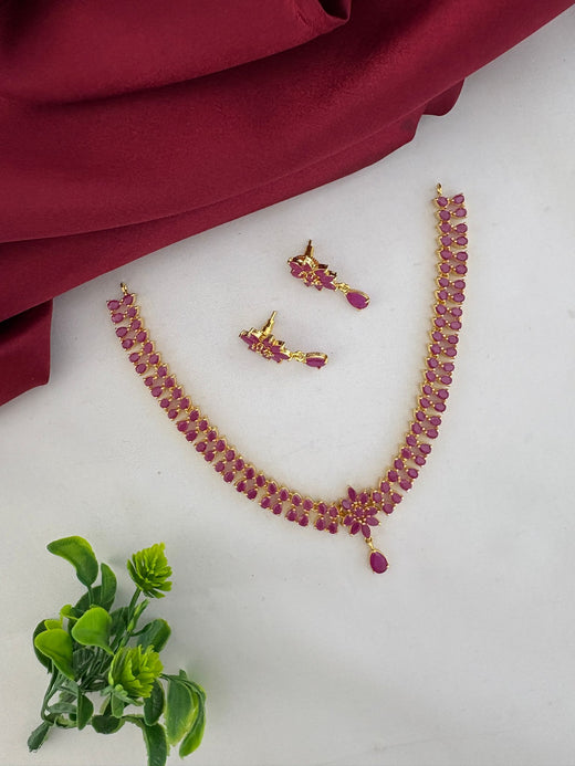 FeelOri Luxury Ruby-Tone CZ Short Necklace Set - Premium South Indian Design. Styled flat lay with a decorative green accent and elegantly curved necklace.