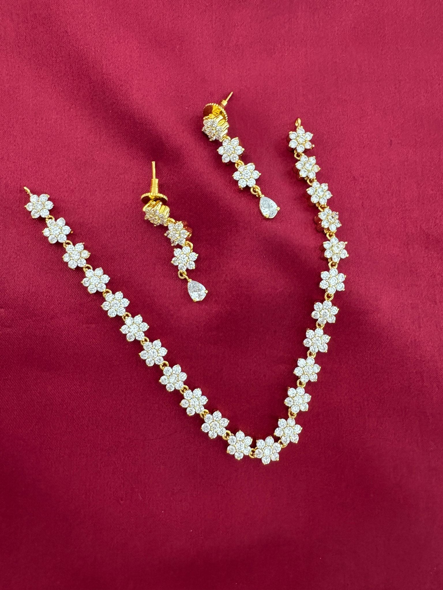 FeelOri Solitaire Sparkle AD Stone Short Necklace Set, detailed view of floral links and earrings on maroon.