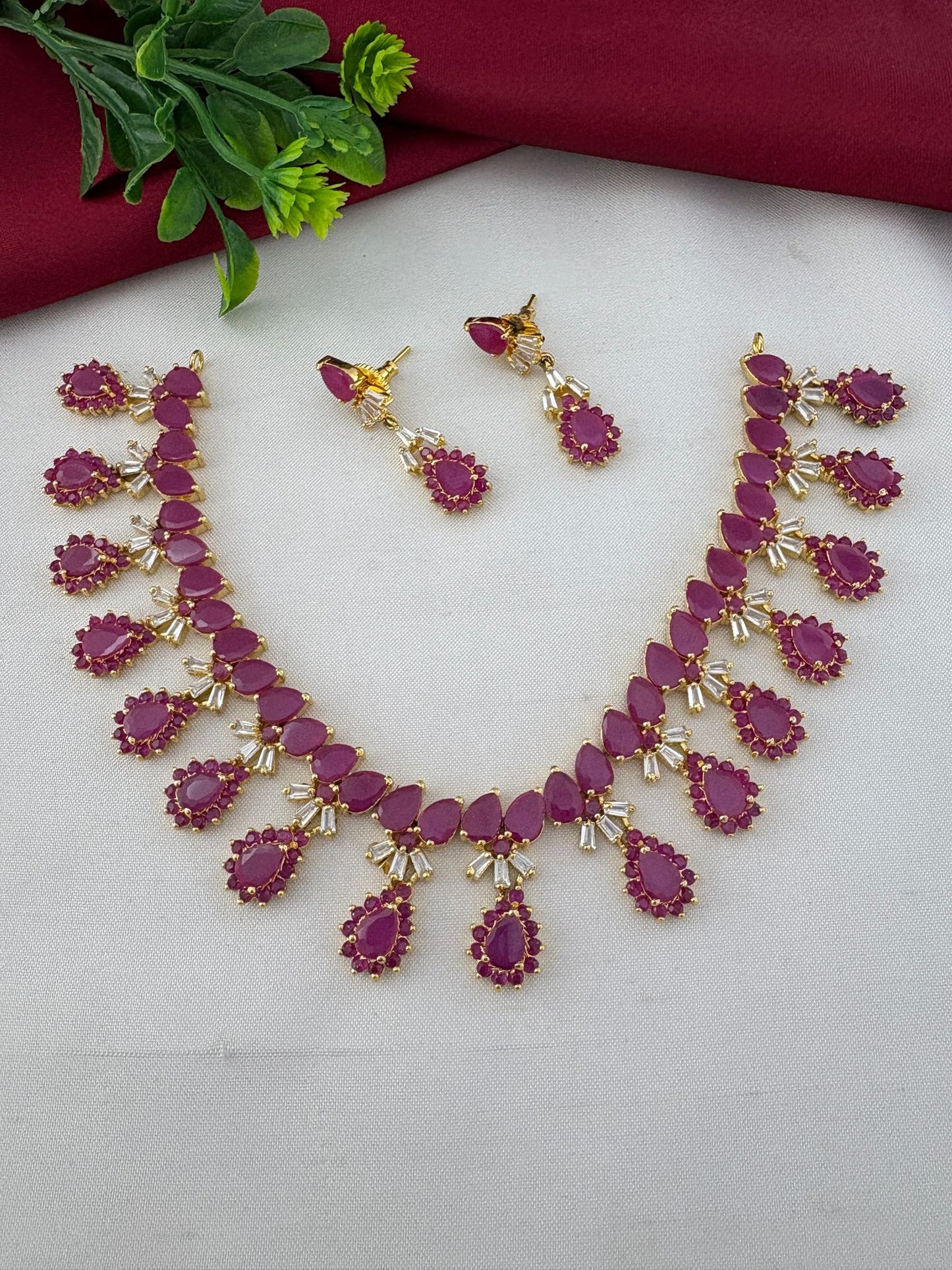 FeelOri South Indian Original Ruby Short Necklace Set displayed with earrings. Styled shot showing the jewellery with a decorative plant element.