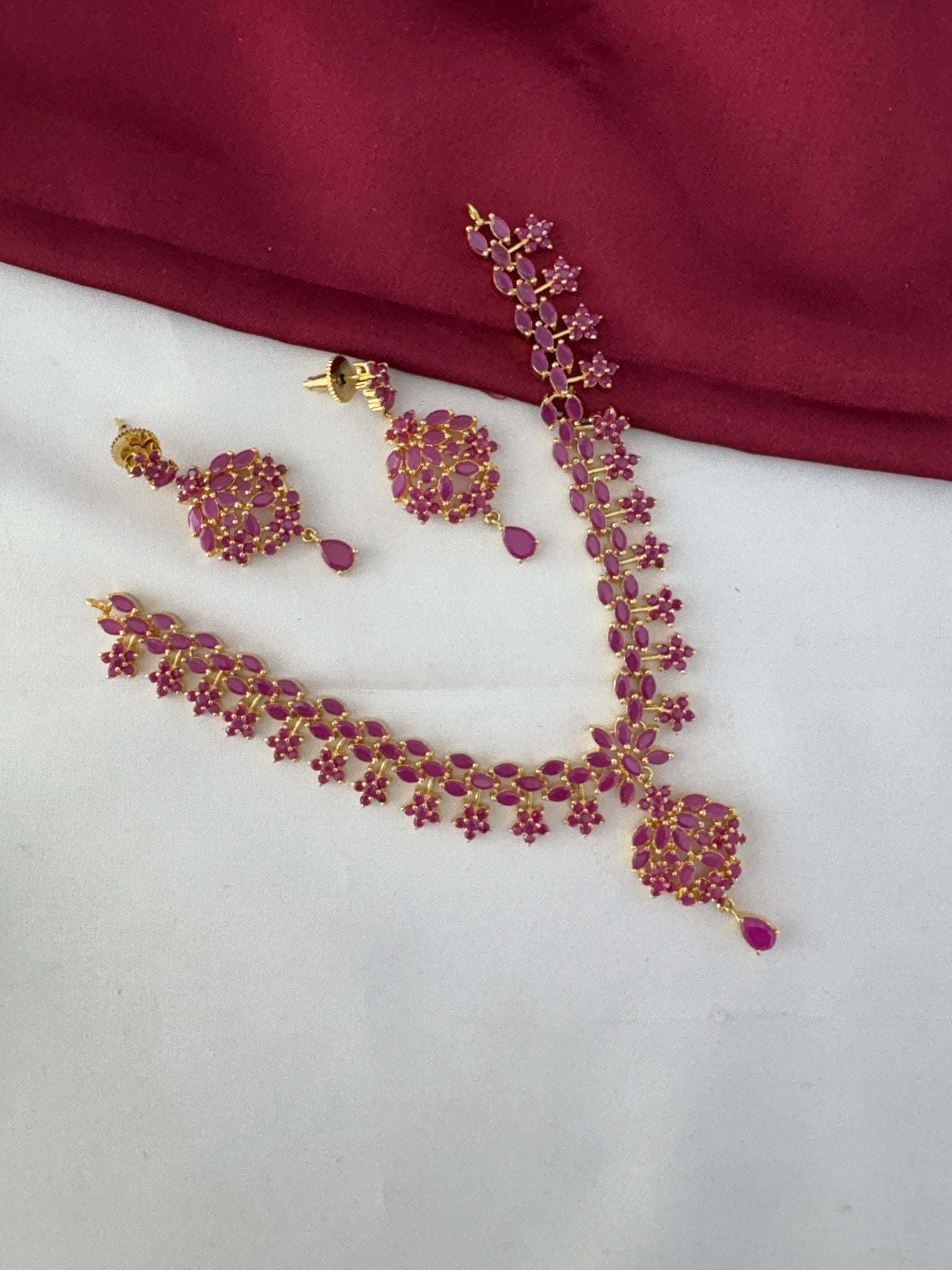 Angled view of the FeelOri Temple Design Ruby-Tone CZ Short Necklace Set and matching earrings, displaying its authentic craft by feelori.