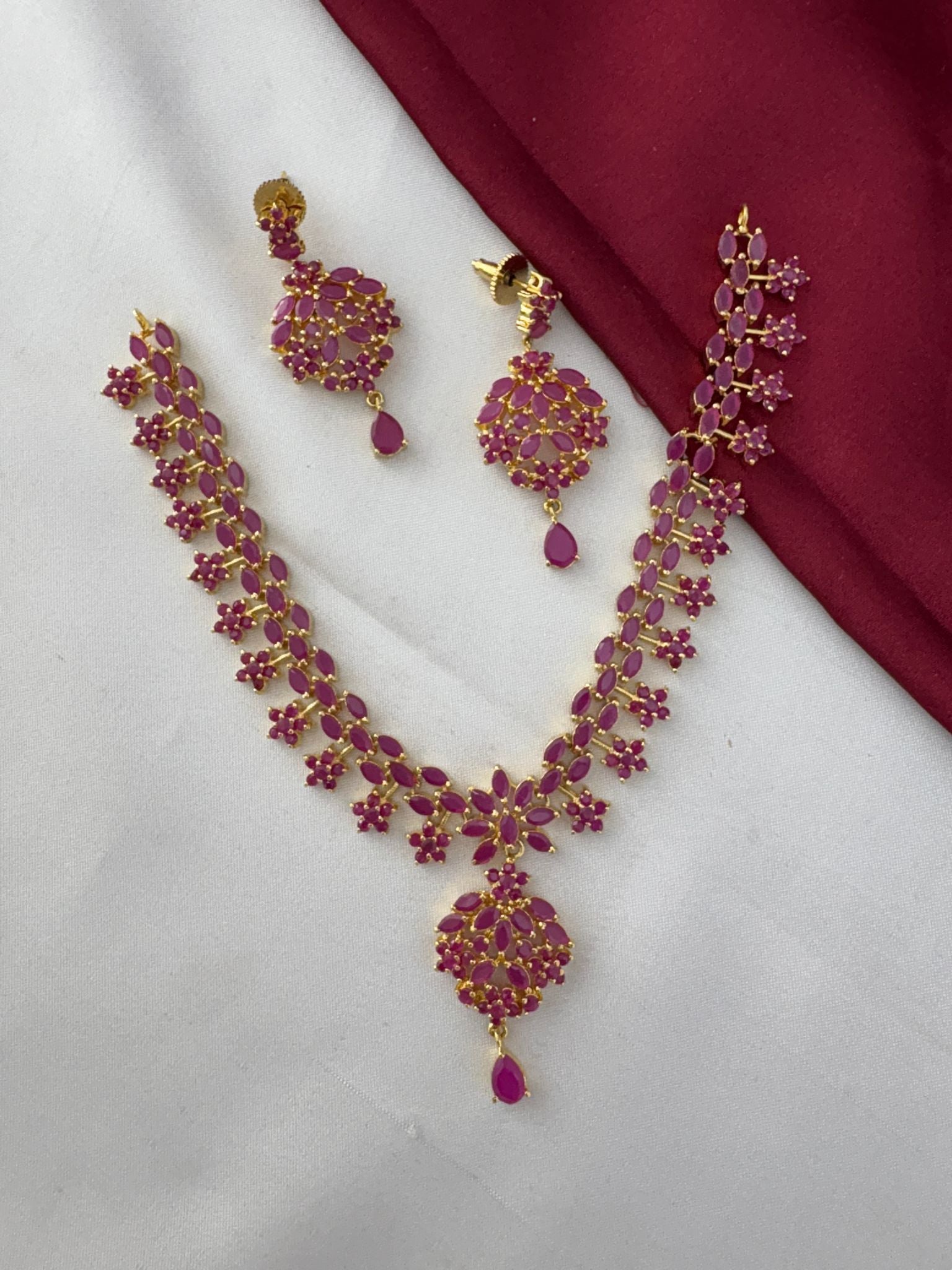 Flatlay of the FeelOri Temple Design Ruby-Tone CZ Short Necklace Set with earrings on a dual-tone background, showcasing authentic craft by feelori.