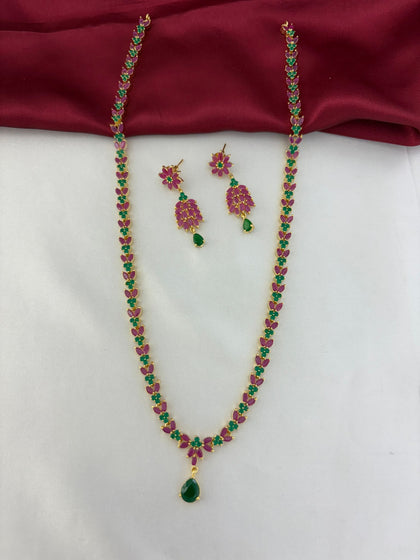 Feelorì Twin Souls Ruby & Emerald Alternating Long Necklace & Earring Set - Full view on maroon and white background.