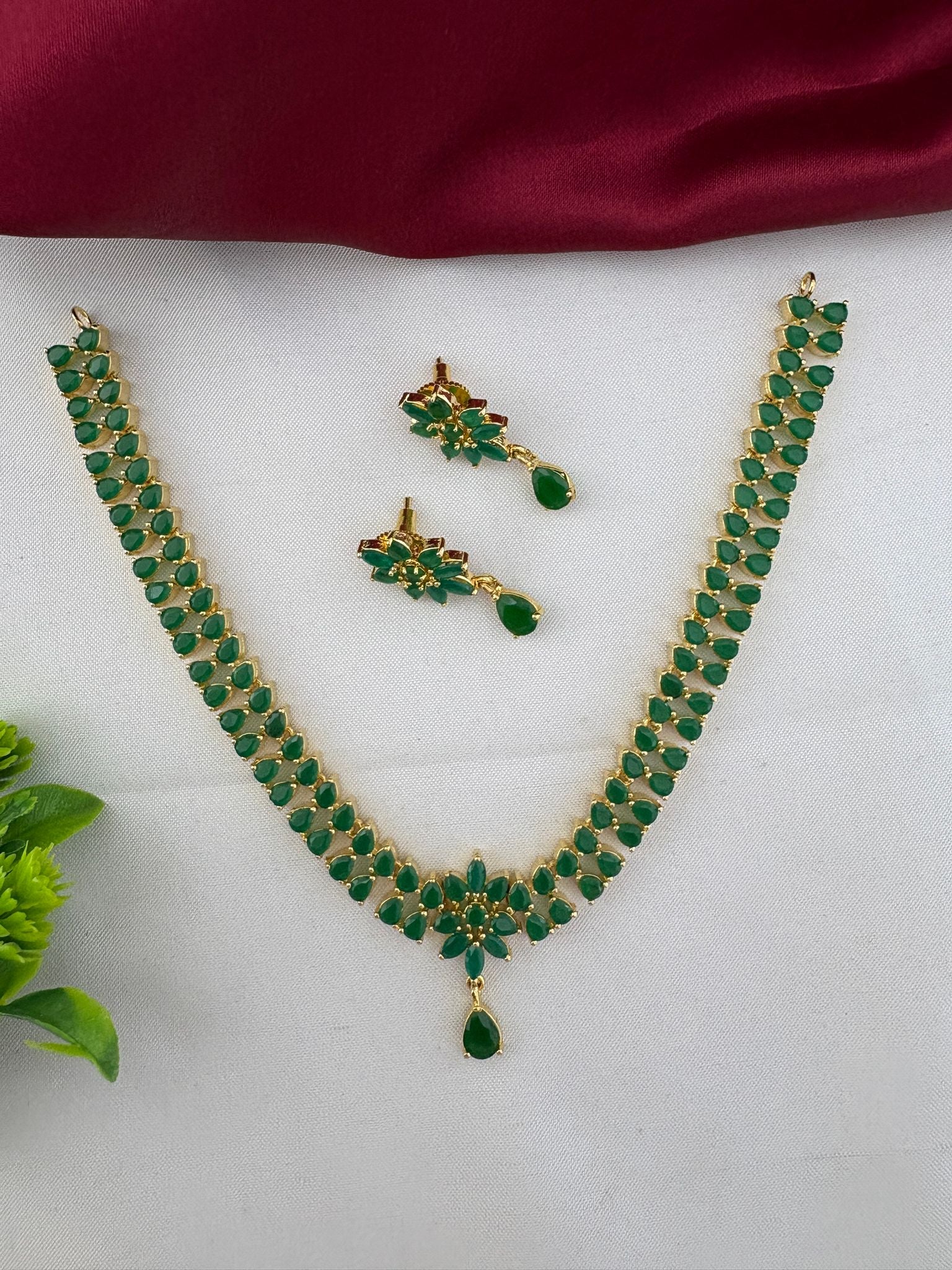 The complete FeelOri Urban Oasis Minimalist Emerald Pendant Set, including necklace and earrings, styled with a subtle green plant accent, perfect for daily chic wear.