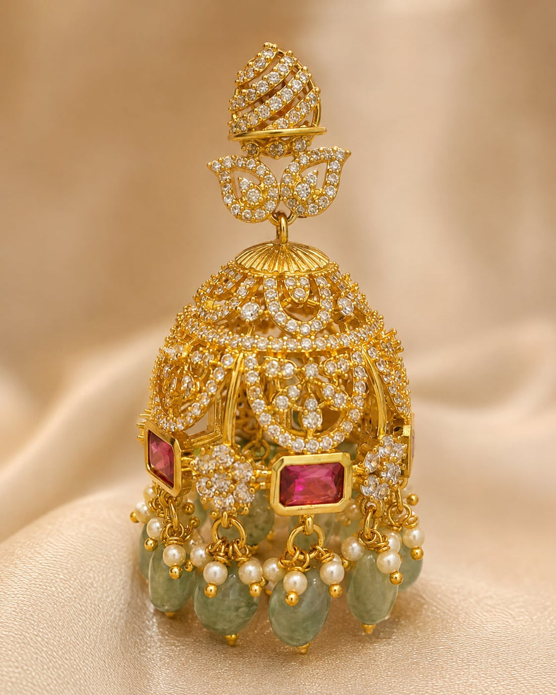 Close-up of gold-plated emerald-drop CZ leaf jhumka earrings showing leaf motifs, clear CZ settings, emerald-green drops and gold bead fringe