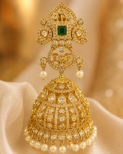 Close-up of grand gold-plated emerald CZ jhumka earrings with pearl-look fringe showing ornate top, emerald-green centre, layered clear CZ work and pearl-look fringe
