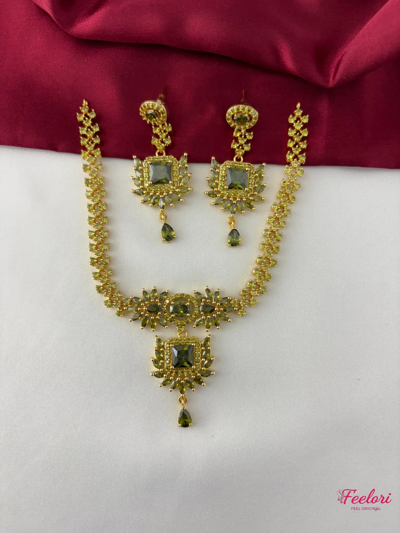 FeelOri Gold Plated Green Stone Necklace Set - Front view showcasing the regal necklace with a central square pendant and matching earrings against a red and white backdrop.