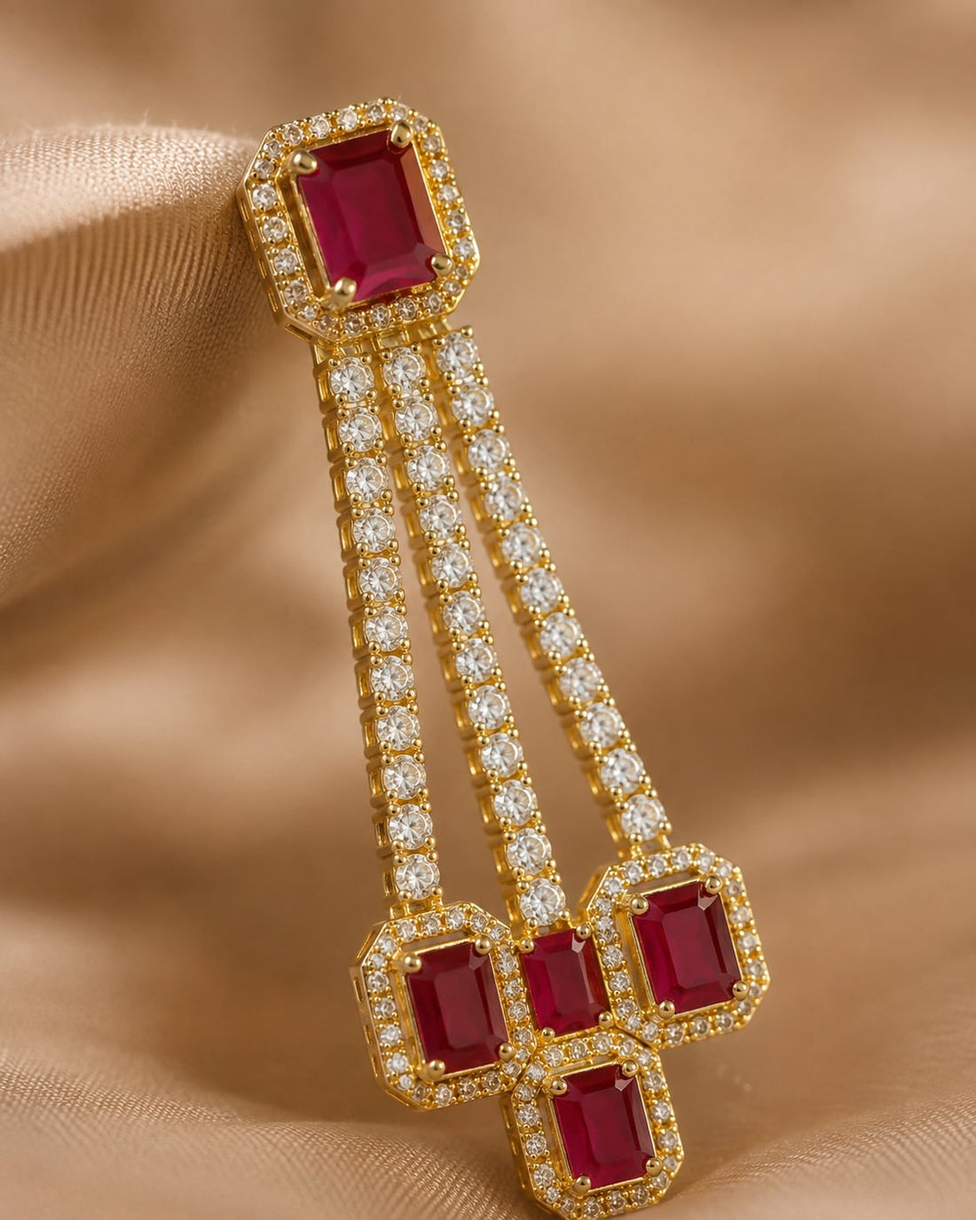 Close-up of gold-plated ruby linear CZ hanging earrings showing ruby-red geometric accents and three parallel clear-CZ strands