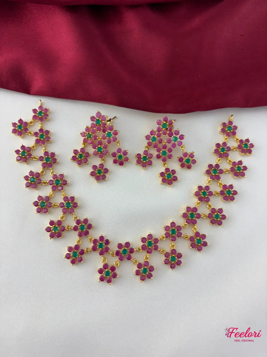 FeelOri Gold Plated Floral Ruby Emerald Necklace Set - Full front view showcasing the matching necklace and chandelier-style earrings with their distinct five-petal floral motifs.