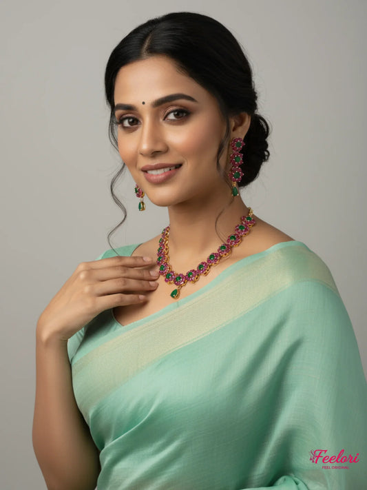 FeelOri Gold Plated Ruby Emerald Floral Necklace Set - Model wears with sage green saree, smiling elegantly.
