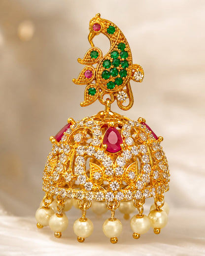 Close-up of gold-plated ruby emerald floral CZ jhumka earrings showing floral top, clear CZ settings, ruby-red and emerald-green accents, and pearl-look fringe