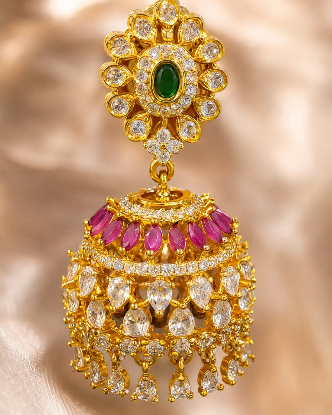 Close-up of gold-plated ruby emerald floral-dome CZ jhumka earrings showing floral stud, ruby-red accents, clear CZ dome and gold bead drops