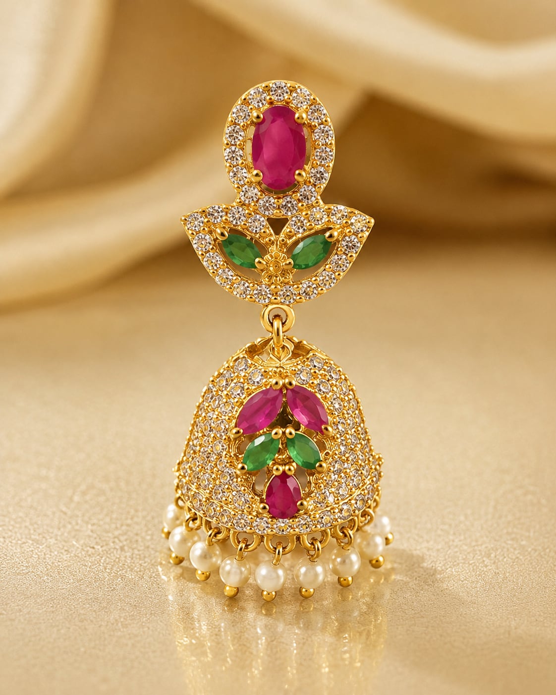 Close-up of petite gold-plated ruby emerald butterfly CZ jhumka earrings showing ruby-red halo top, butterfly connector, emerald-green accents and pearl-look fringe