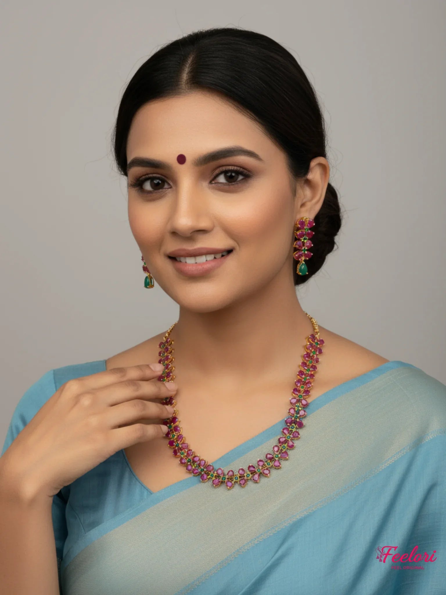 FeelOri Gold Plated Ruby Emerald Leaf Motif Necklace Set - Model wearing set with blue traditional saree, smiling.