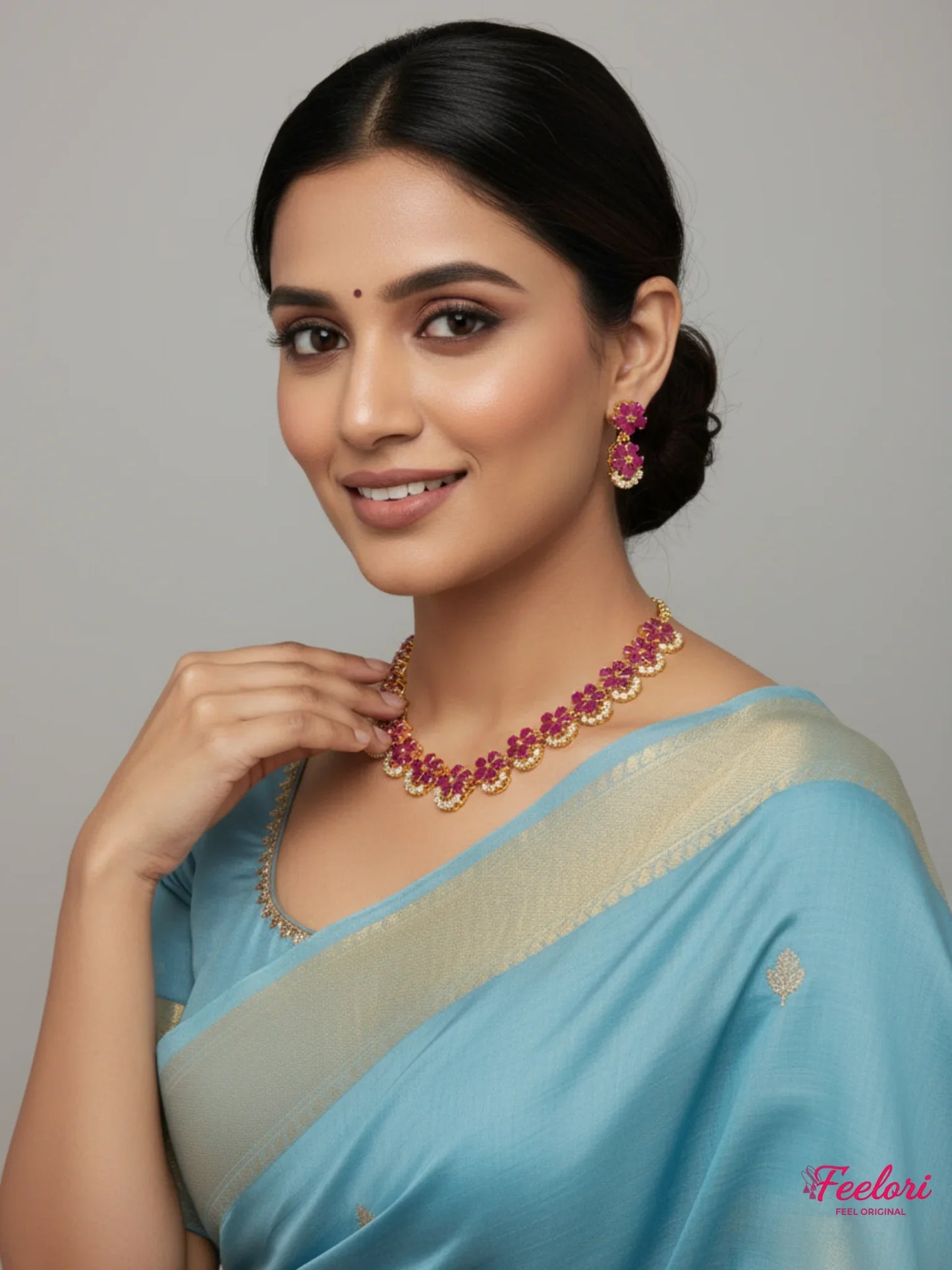 FeelOri Gold Plated Ruby Floral Necklace Set - Model in light blue saree smiling at camera.