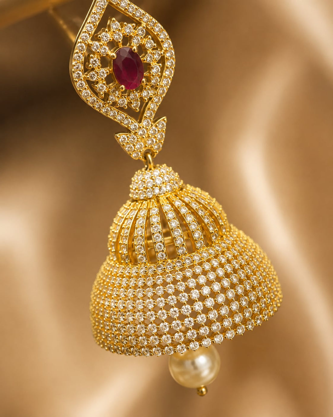 Close-up of gold-plated ruby paisley CZ bell jhumka earrings showing ruby-red paisley tops, clear CZ bell domes and pearl-look drops